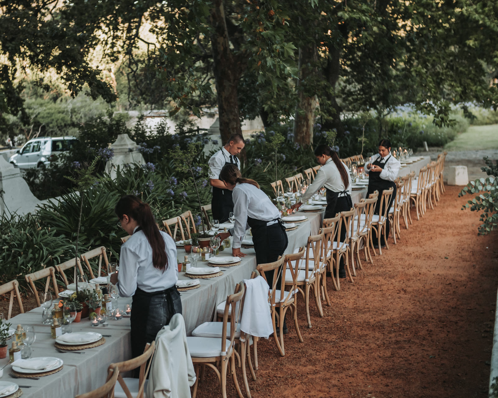 Staff adjusting place settings on an outdoor dining table